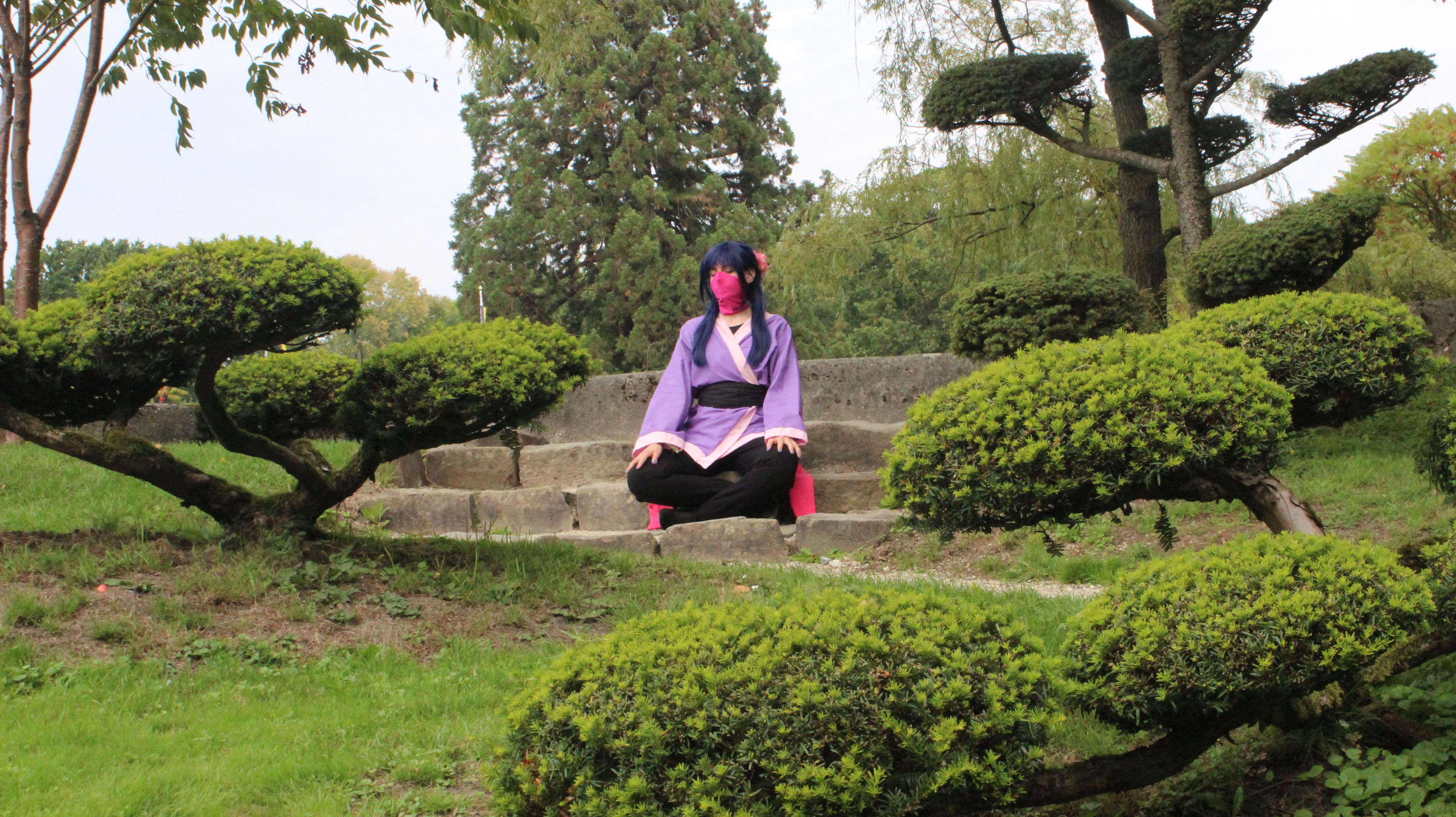 An image of a Watcher cosplayer in a cross-legged meditation pose surrounded by nature.