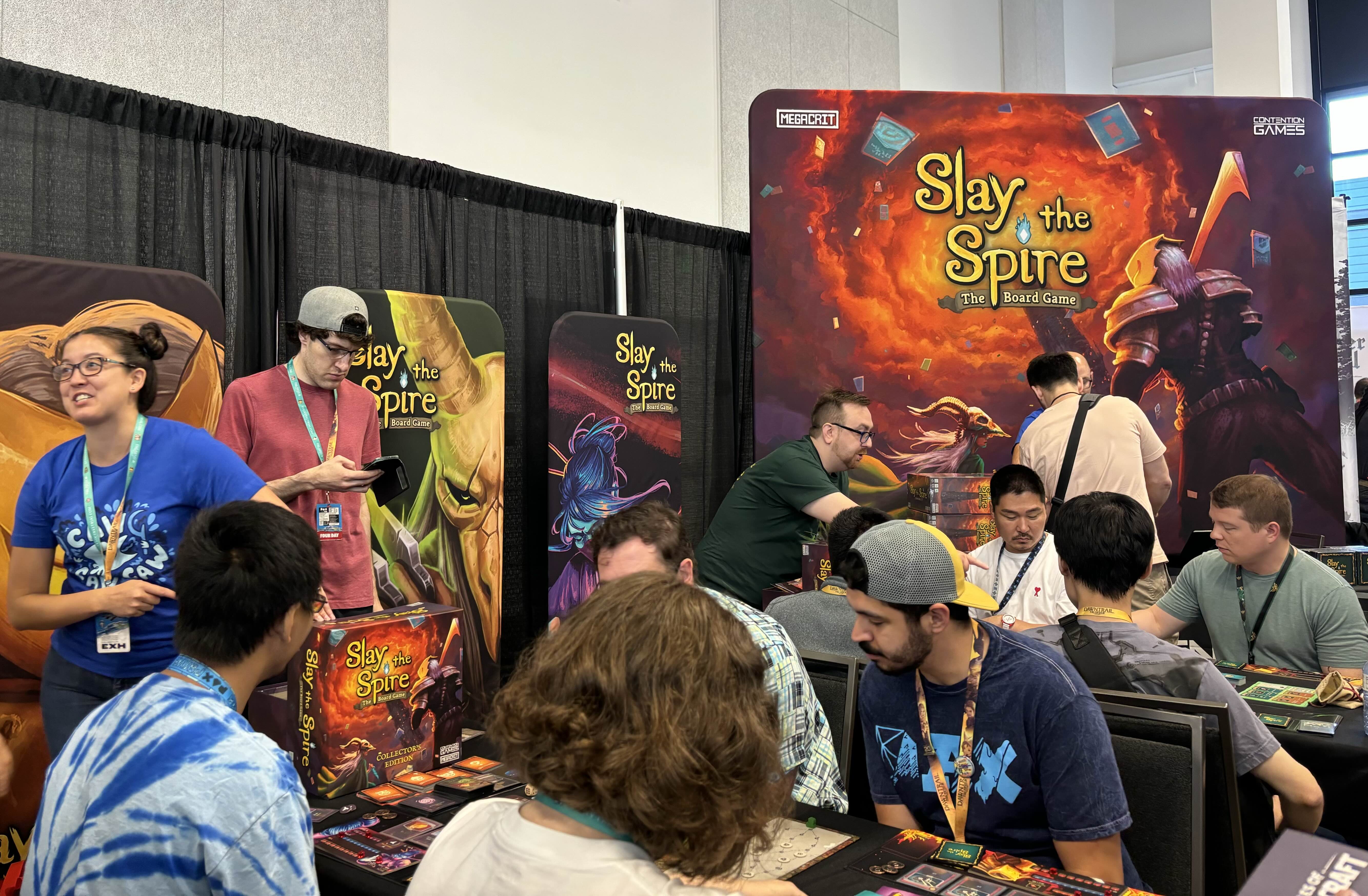 An image of Contention Games&rsquo; booth at PAX West, with big Slay the Spire banners and lots of players sitting at tables demoing the board game.