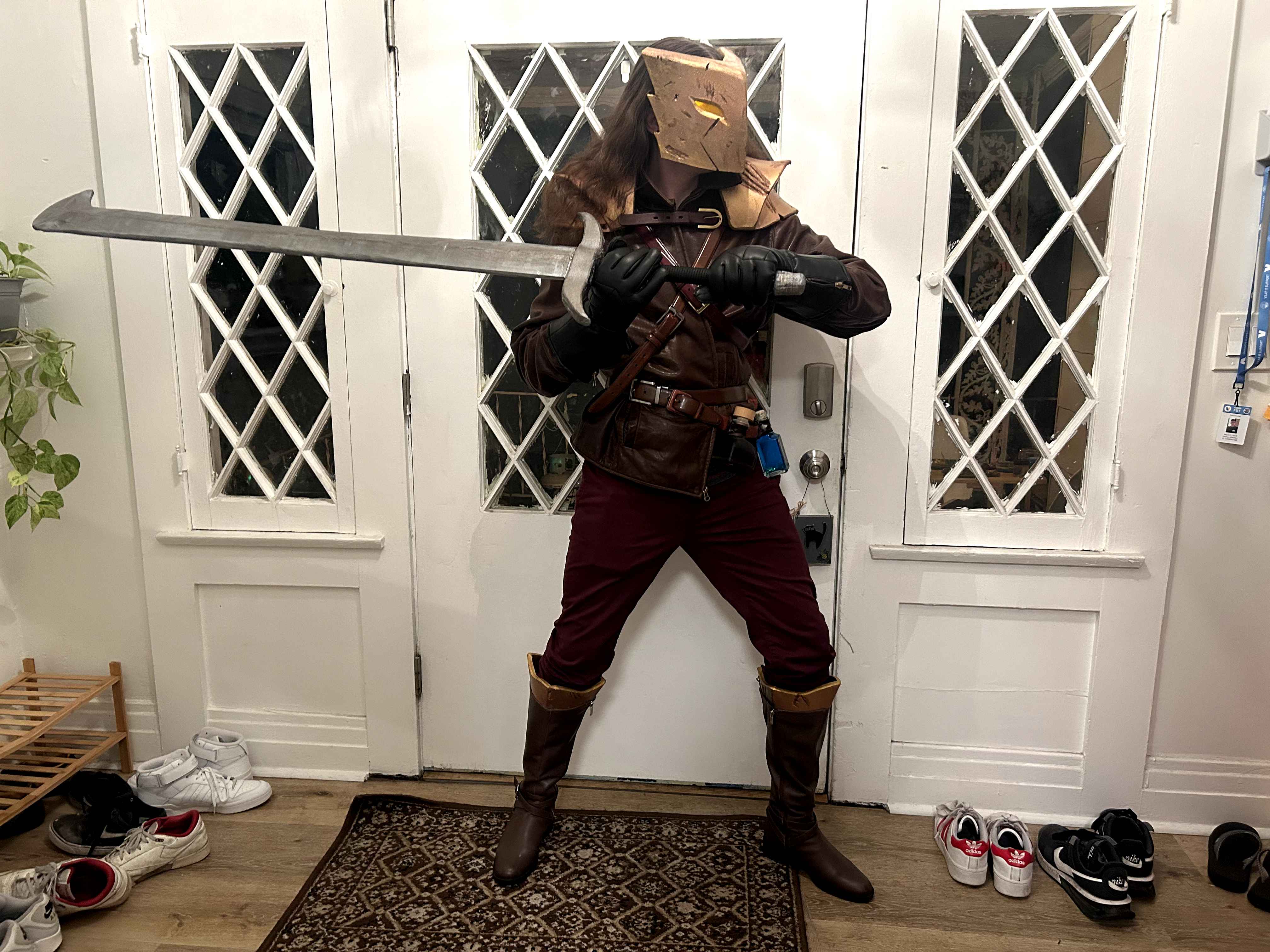 A cosplay of The Ironclad with a leathery vest, potion belt, shiny pauldrons and mask with glowing eyes, signature sword, red pants, and leathery boots, with the cosplayer in Ironclad&rsquo;s iconic combat pose.